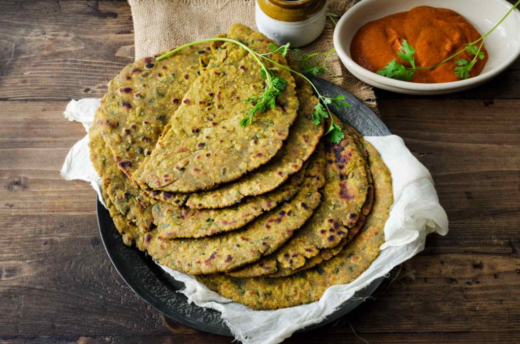 Bajra Aloo Roti is prepared with a mix of bajra flour, mashed potatoes, ginger garlic paste, coriander leaves, garam masala. It is served hot with white butter with raita as accompaniments. It tastes heavenly and just melts in the mouth.